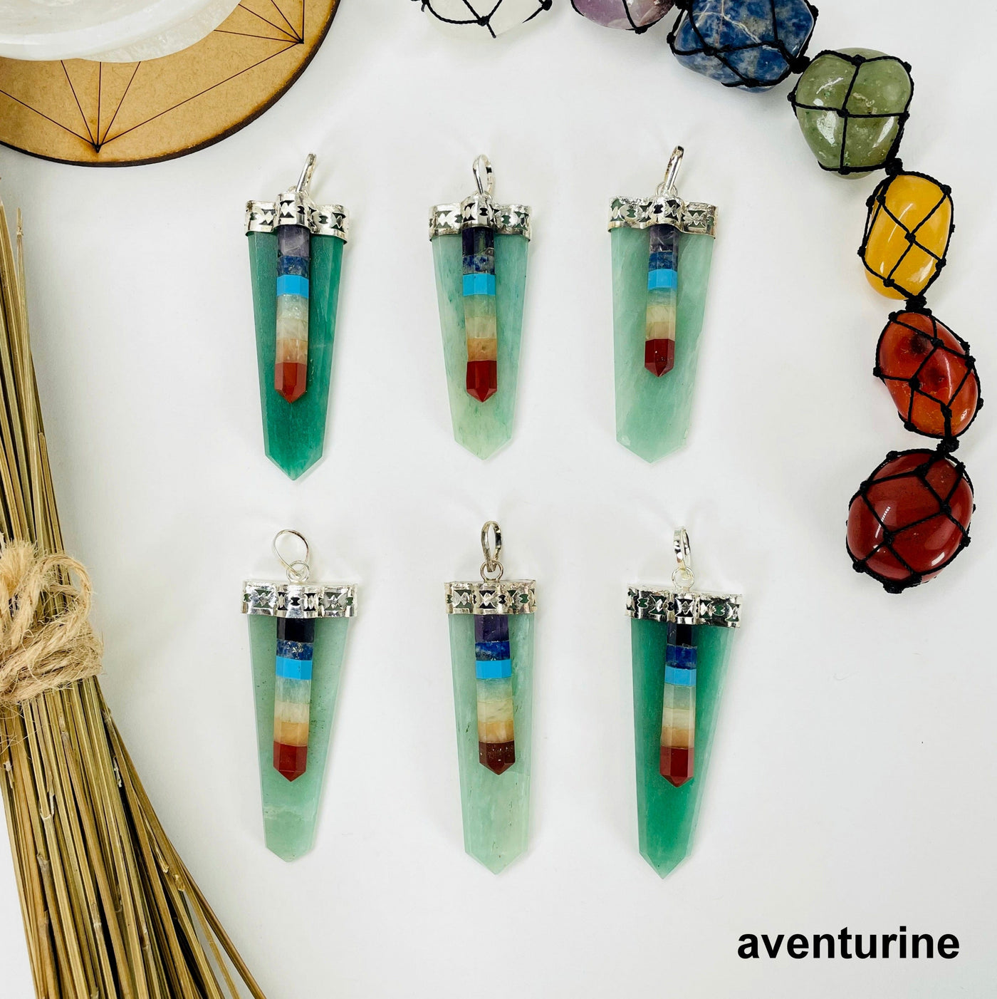 overhead view of six aventurine polished point pendants with chakra point accents on white background with decorations for possible variations
