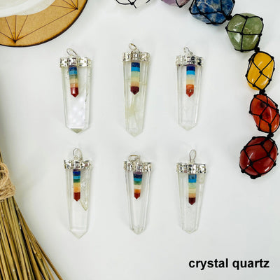 overhead view of six crystal quartz polished point pendants with chakra point accents on white background with decorations for possible variations