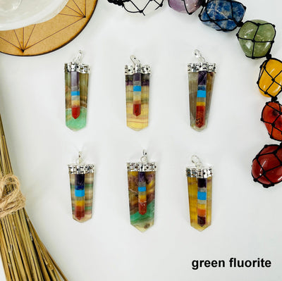overhead view of six green fluorite polished point pendants with chakra point accents on white background with decorations for possible variations
