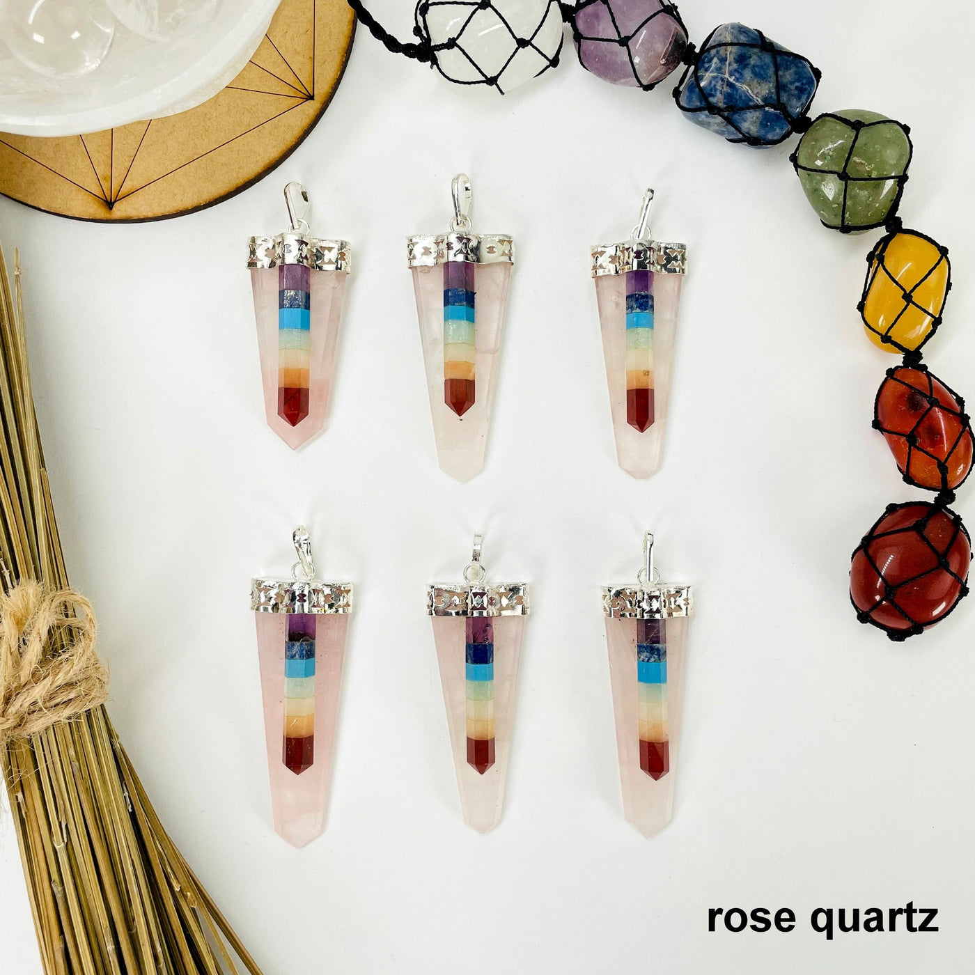 overhead view of six rose quartz polished point pendants with chakra point accents on white background with decorations for possible variations