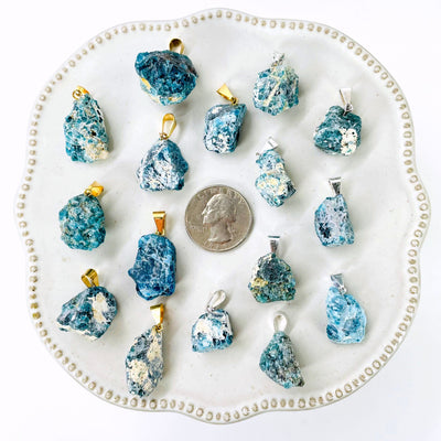 many gold and silver raw blue apatite chunk pendants on display with a quarter for size reference