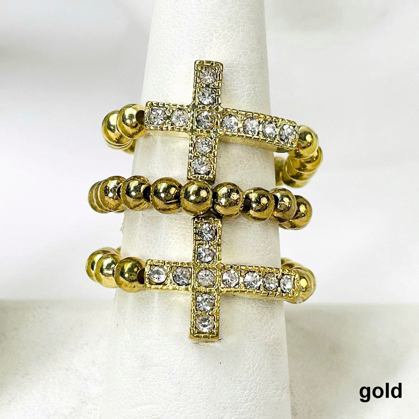 close up of three gold sideways cross elastic rings on ring display