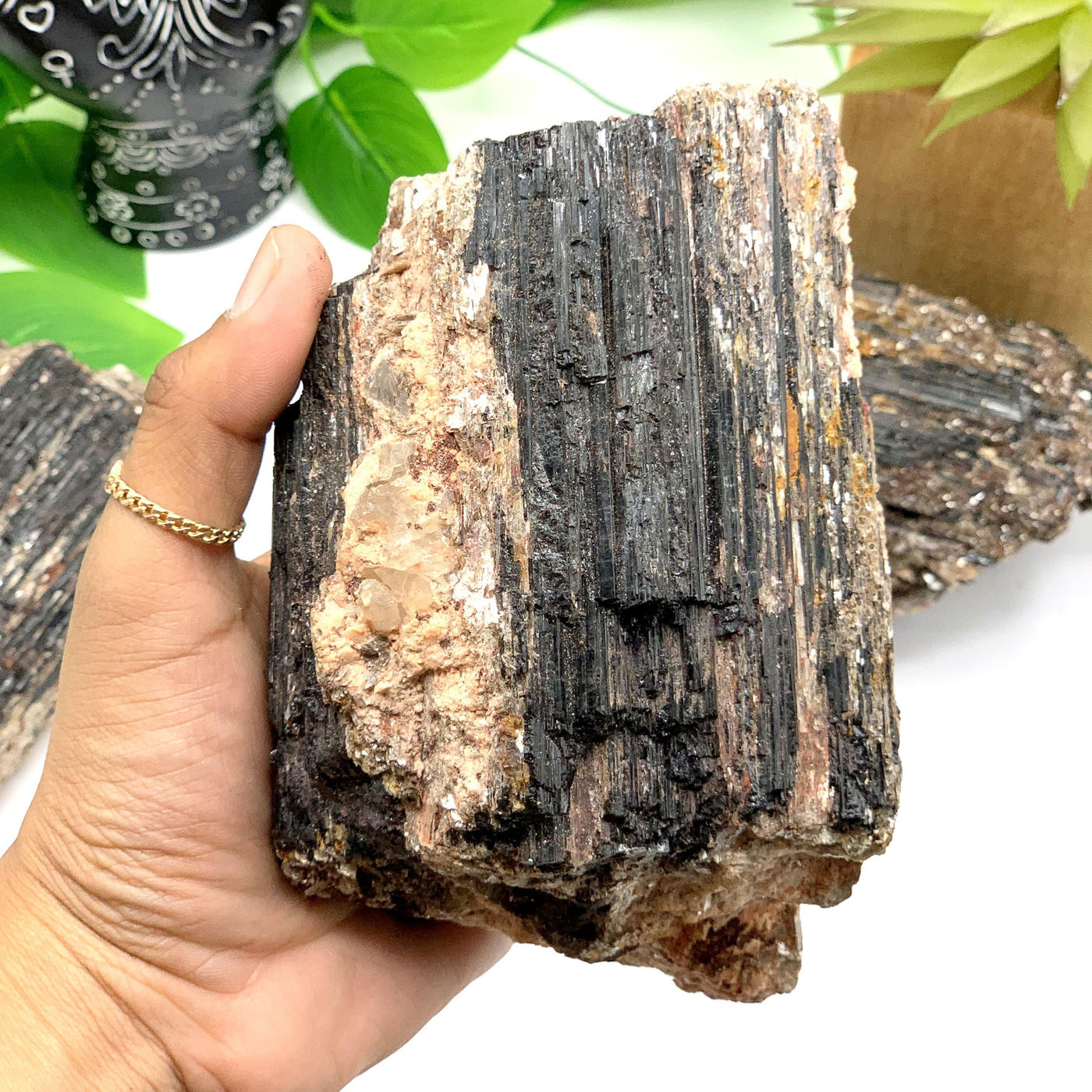 hand holding up Black Tourmaline with Mica on Matrix with decorations in the background