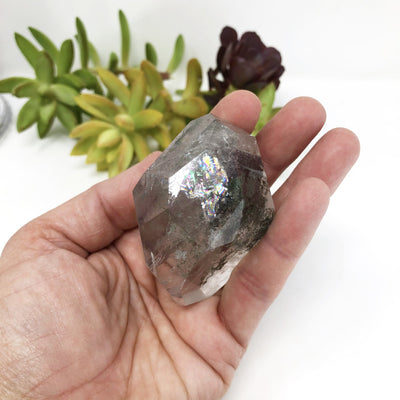 hand holding up Crystal Quartz Cut and Polished Freeform Stone with Chlorite Inclusions with decorations in the background