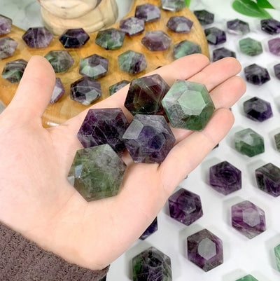 hand holding up hexagonal fluorite polished stones with decorations in the background