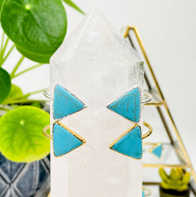 one gold and one silver turquoise howlite double triangle adjustable bracelet on crystal quartz point in front of background decorations for finish comparison