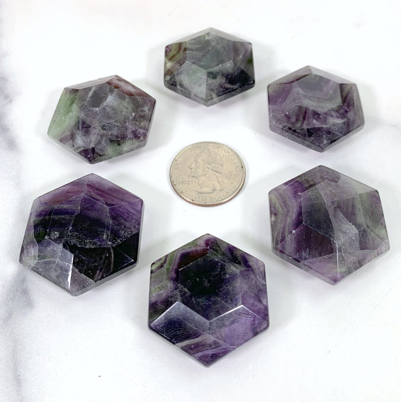 6 hexagonal fluorite polished stones surrounding a quarter for size reference on white background