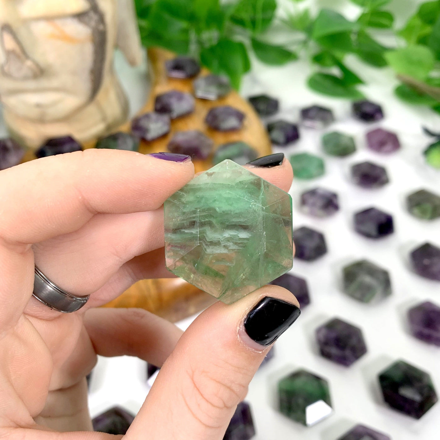 hand holding up hexagonal fluorite polished stone with decorations blurred in the background