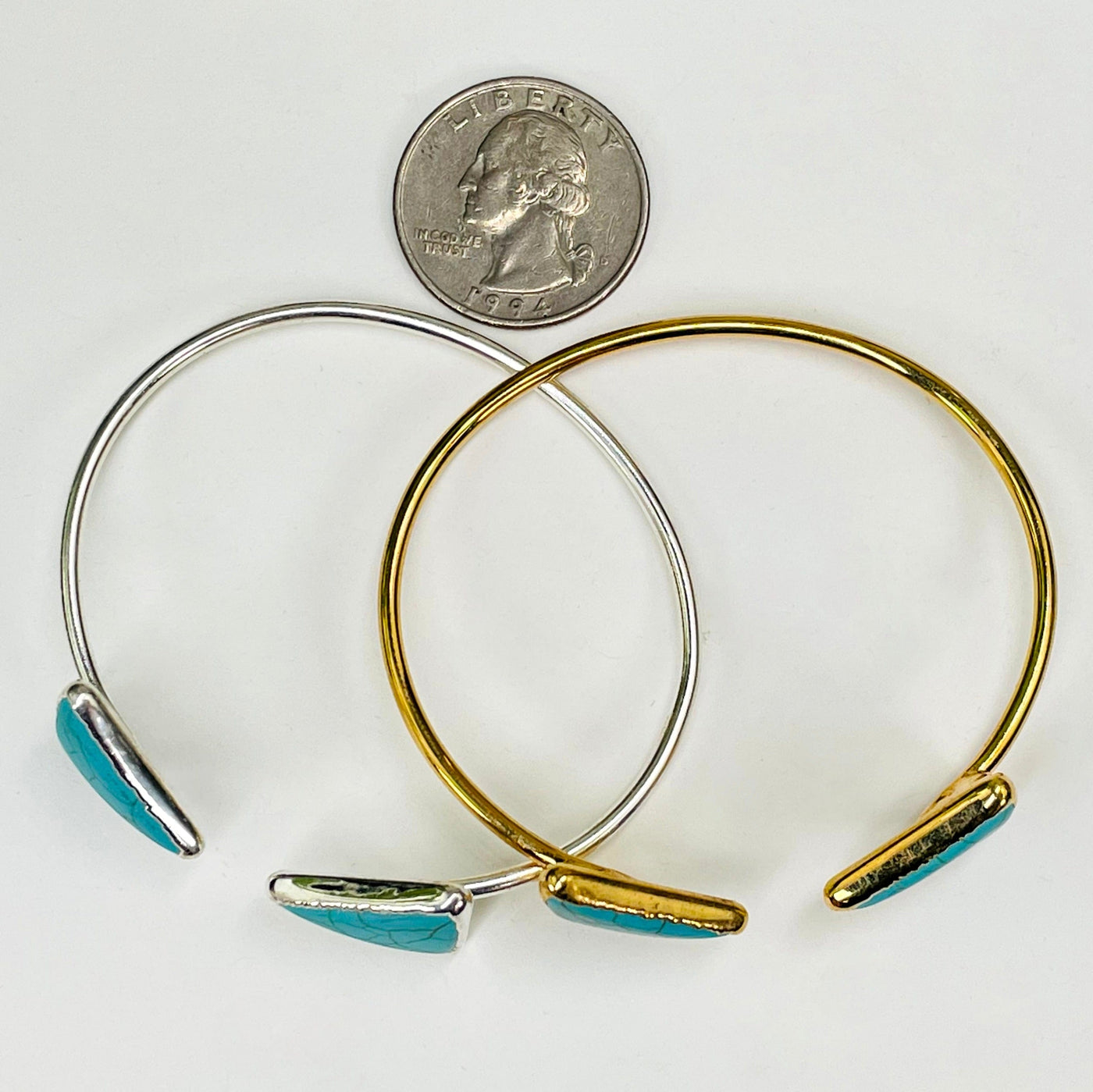 overhead view of one gold and one silver turquoise howlite double triangle adjustable bracelets with a quarter for size reference