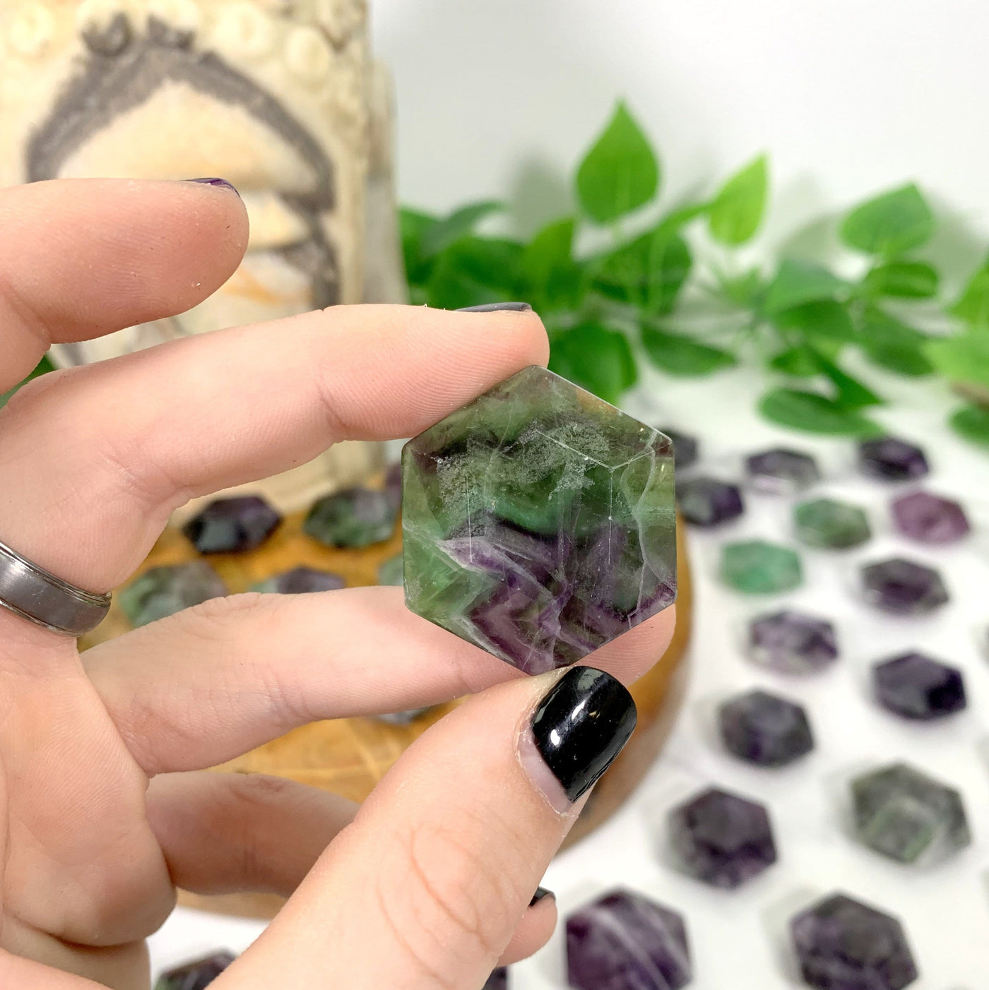 hand holding up hexagonal fluorite polished stone with decorations blurred in the background