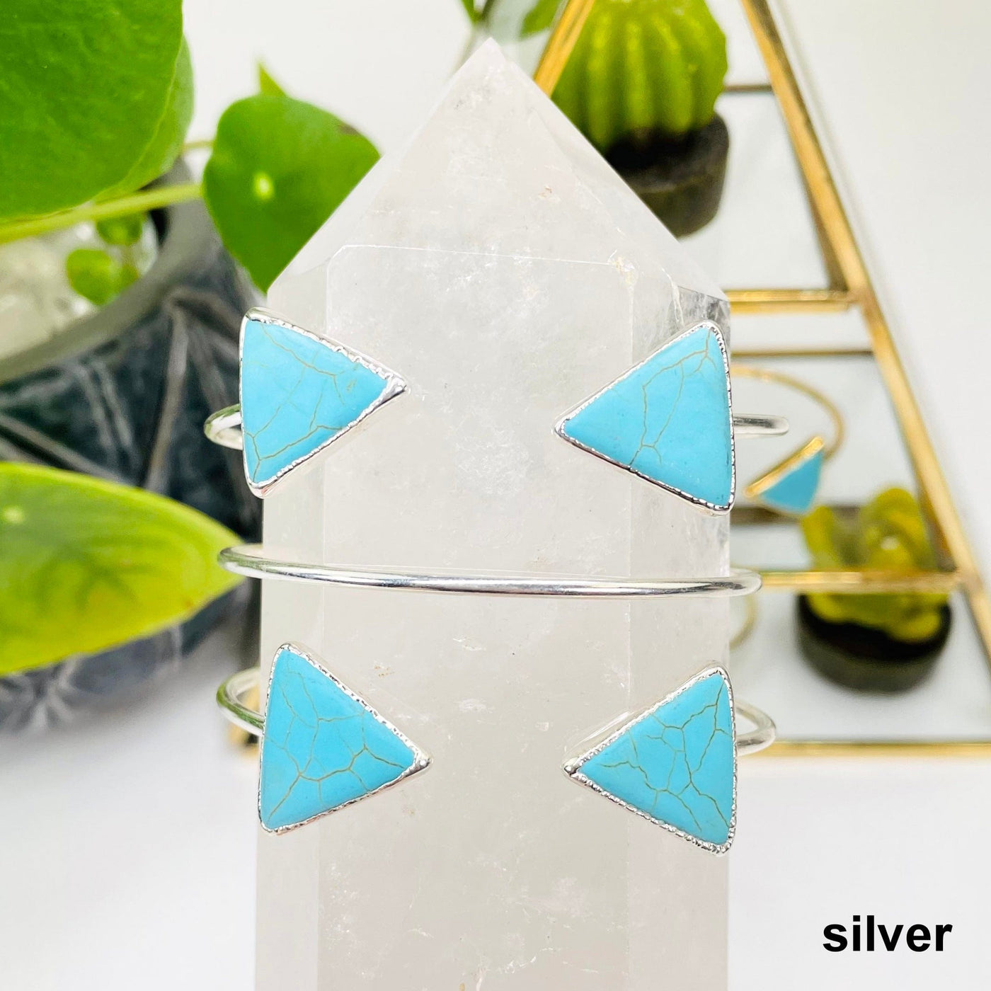 two silver turquoise howlite double triangle adjustable bracelets facing forward and one facing backwards on crystal quartz point in front of background decorations
