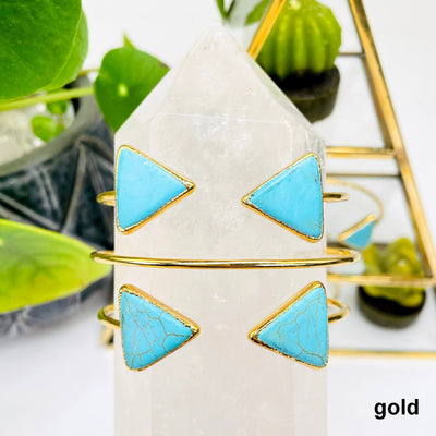 two gold turquoise howlite double triangle adjustable bracelets facing forward and one facing backwards on crystal quartz point in front of background decorations