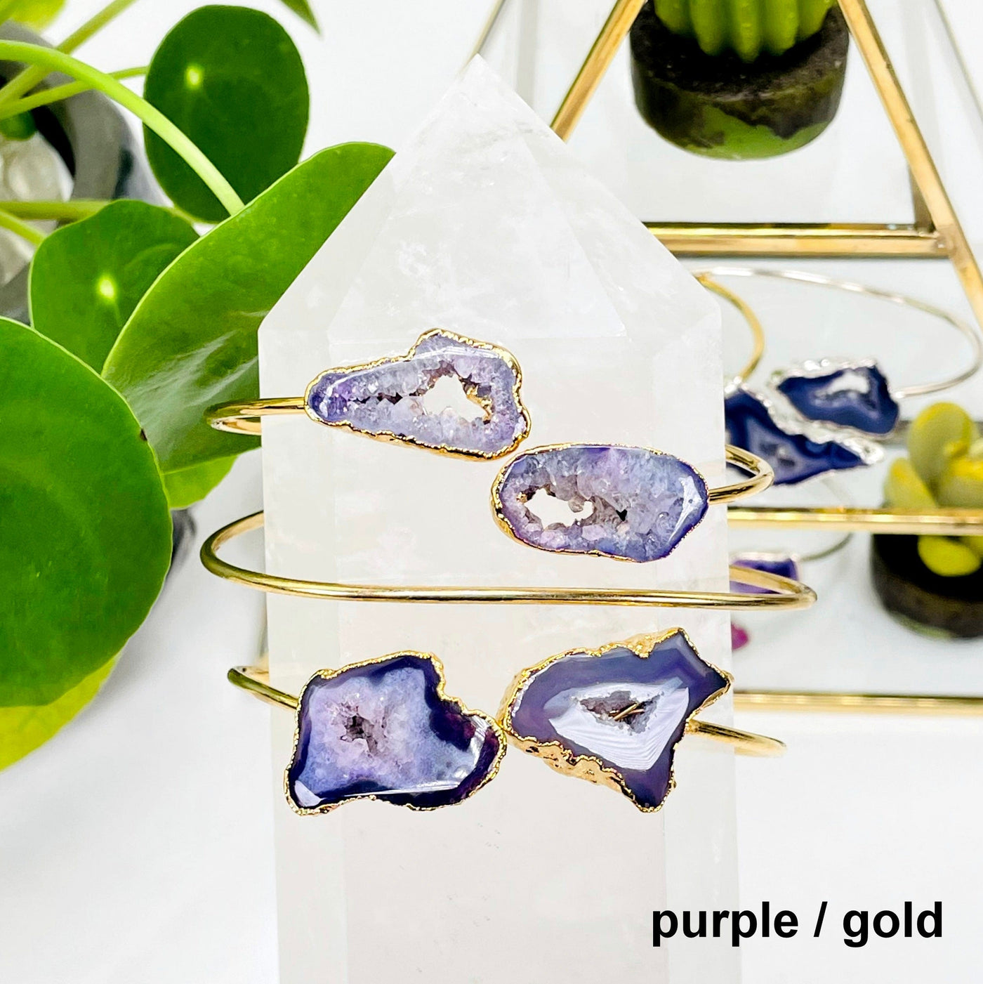 two purple / gold double agate adjustable bracelets facing forward and one facing backwards on a crystal quartz point in front of background decorations