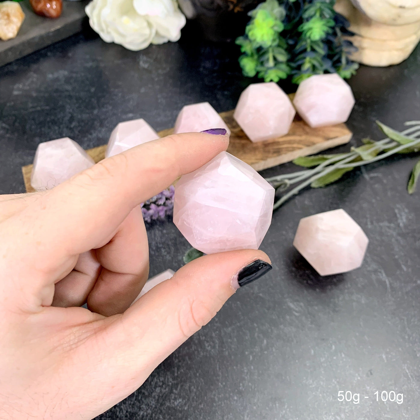 Hand holding up 50-100g Rose Quartz Dodecahedron with others in the background with decorations