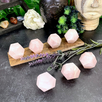5 Rose Quartz Dodecahedrons on a wood slab with 3 others in front of them with decorations