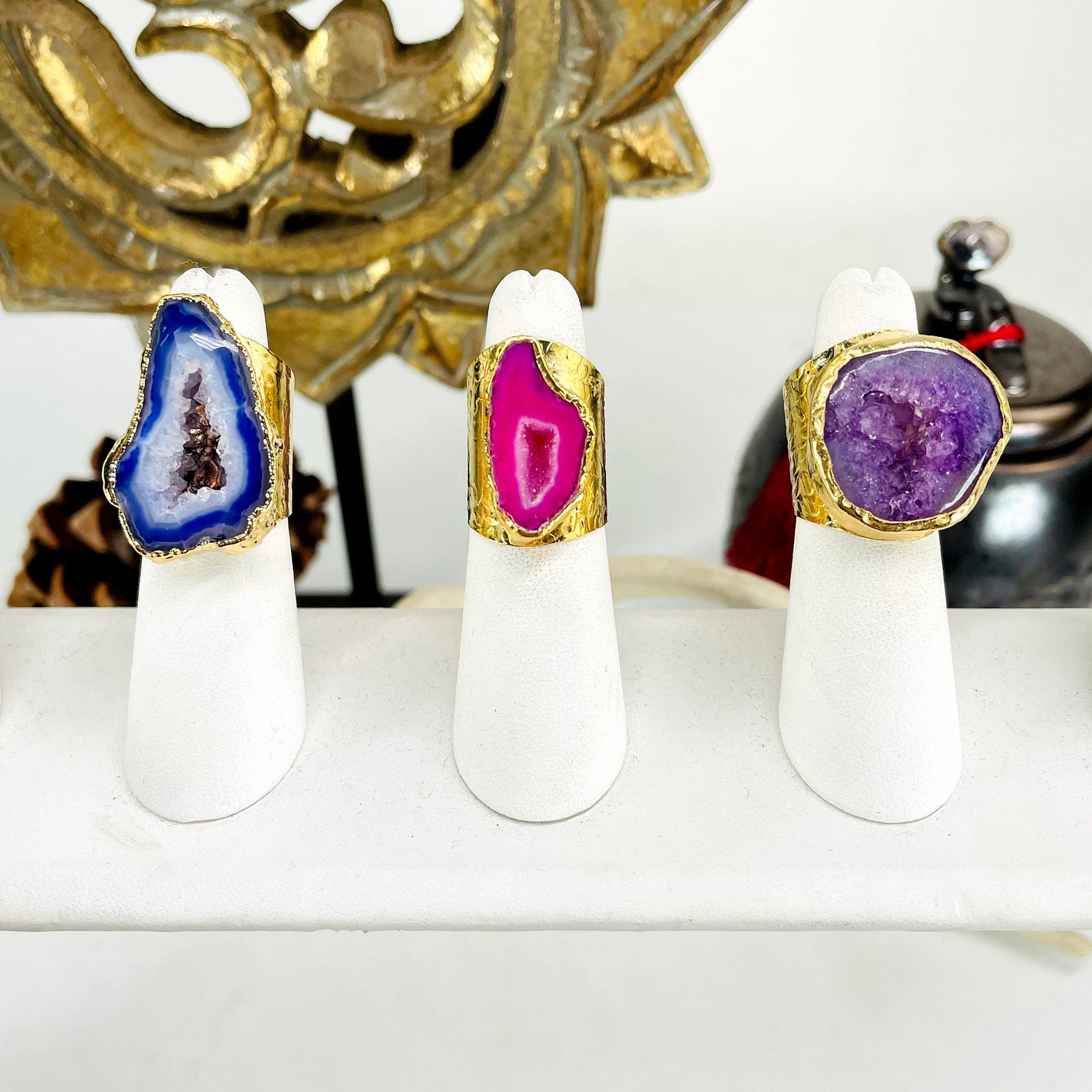 one of each colored agate druzy gold adjustable ring options on ring display in front of background decorations for color comparison