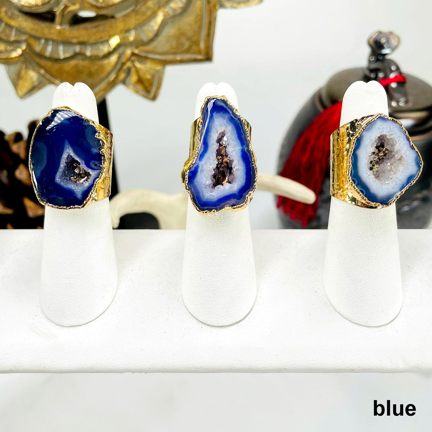 three blue agate druzy gold adjustable rings on ring display in front of background decorations for possible variations 