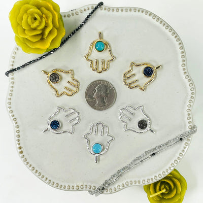 one of each hamsa hand pendant options on display surrounding a quarter for size reference