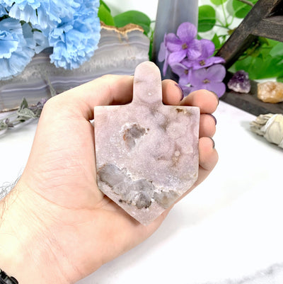 hand holding up Pink Amethyst Druzy Dreidel with decorations in the background