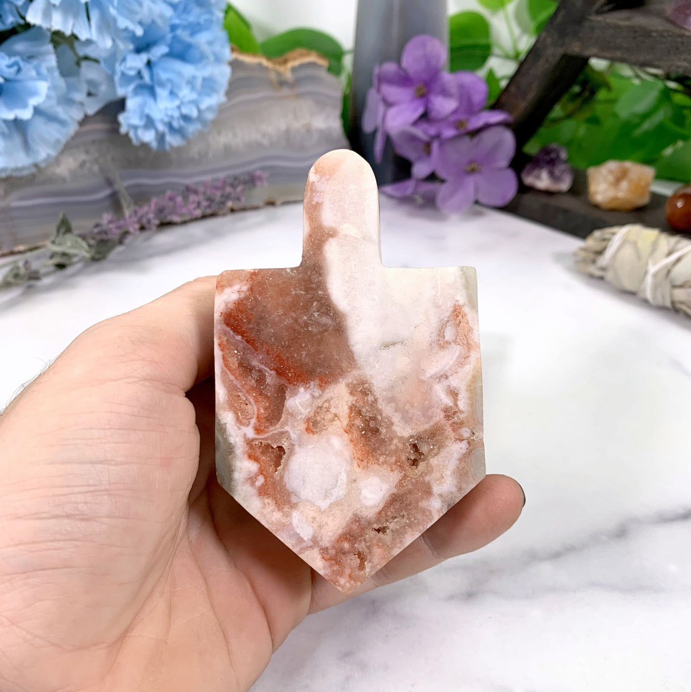 hand holding up Pink Amethyst Druzy Dreidel with decorations in the background