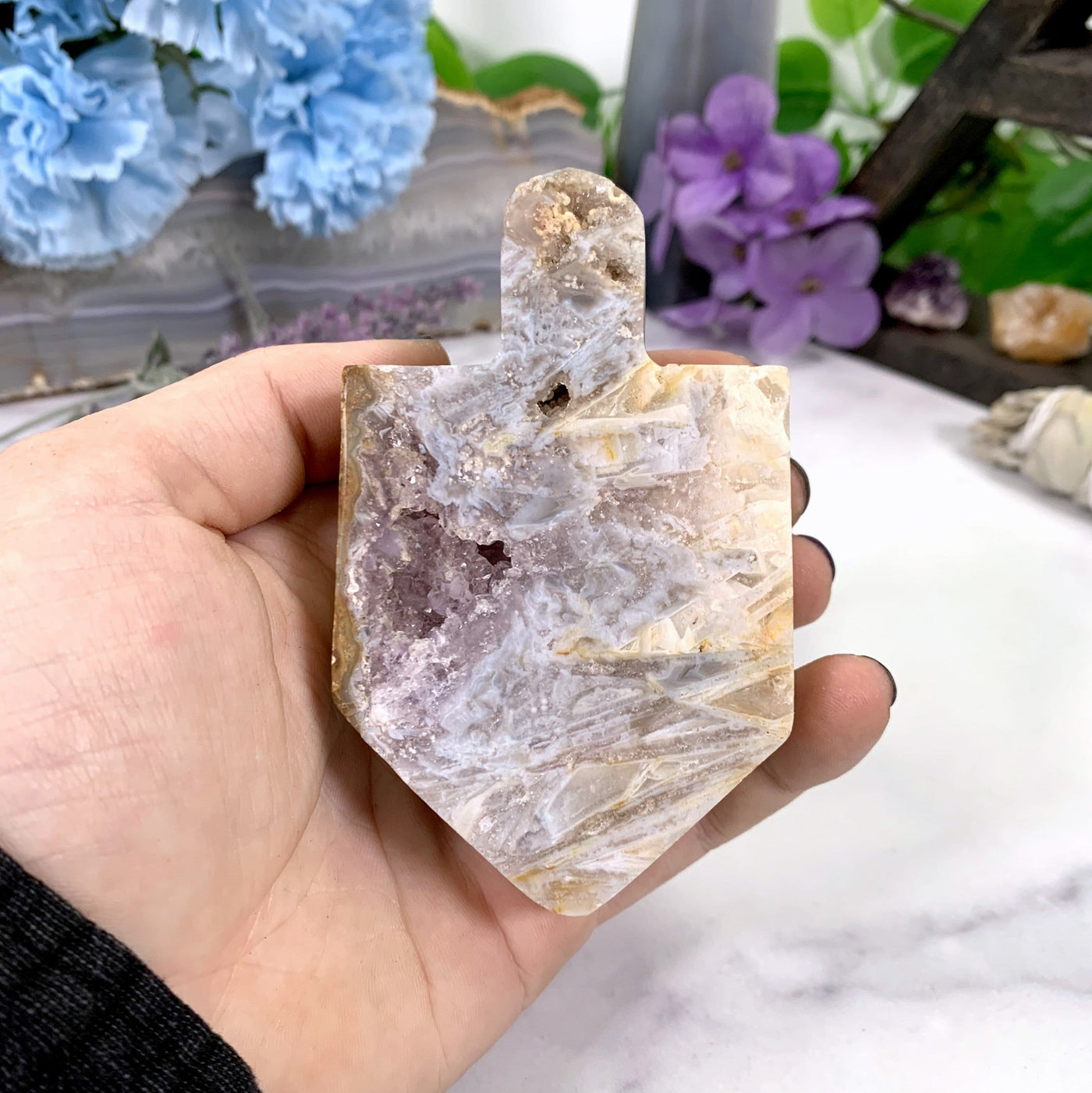 hand holding up Pink Amethyst Druzy Dreidel with decorations in the background