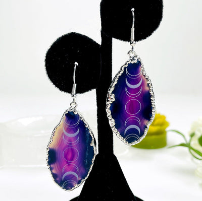 close up of one silver pair of purple agate moon phase dangle earrings on earring display for details