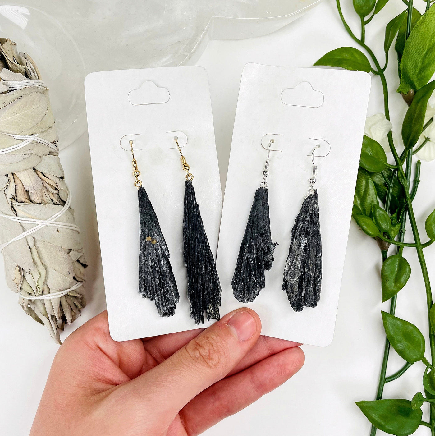 one gold and one silver black kyanite fan dangle earring pairs in their packaging in hand for size reference and finish comparison