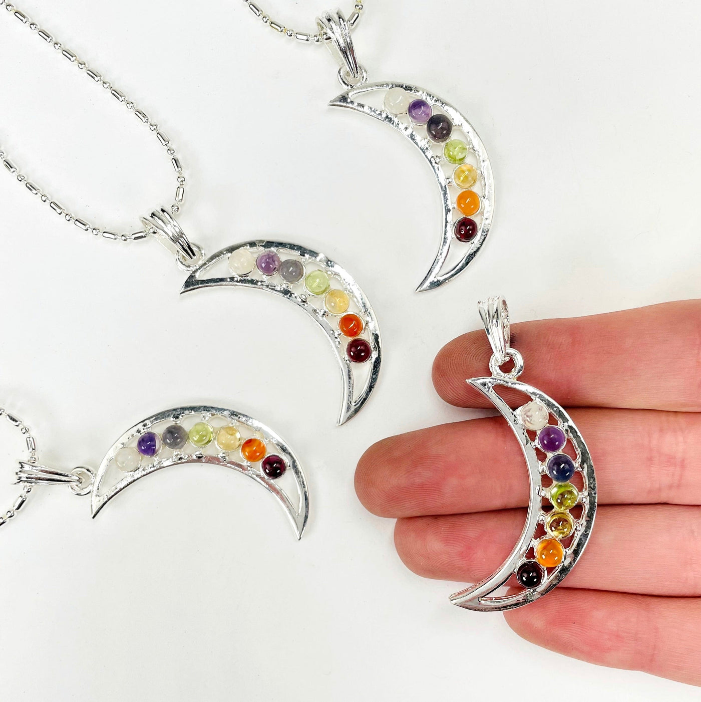 one chakra crescent moon pendant necklace in hand with three others in the background
