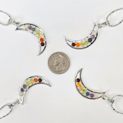 four chakra crescent moon pendant necklaces surrounding a quarter for size reference