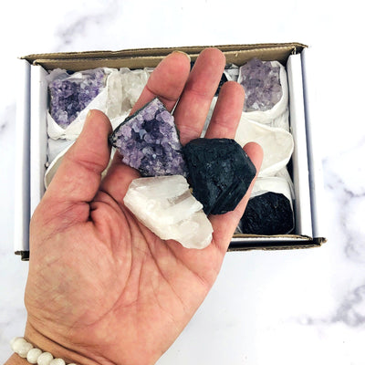 hand holding up amethyst, crystal quartz, and tourmaline clusters in front of box