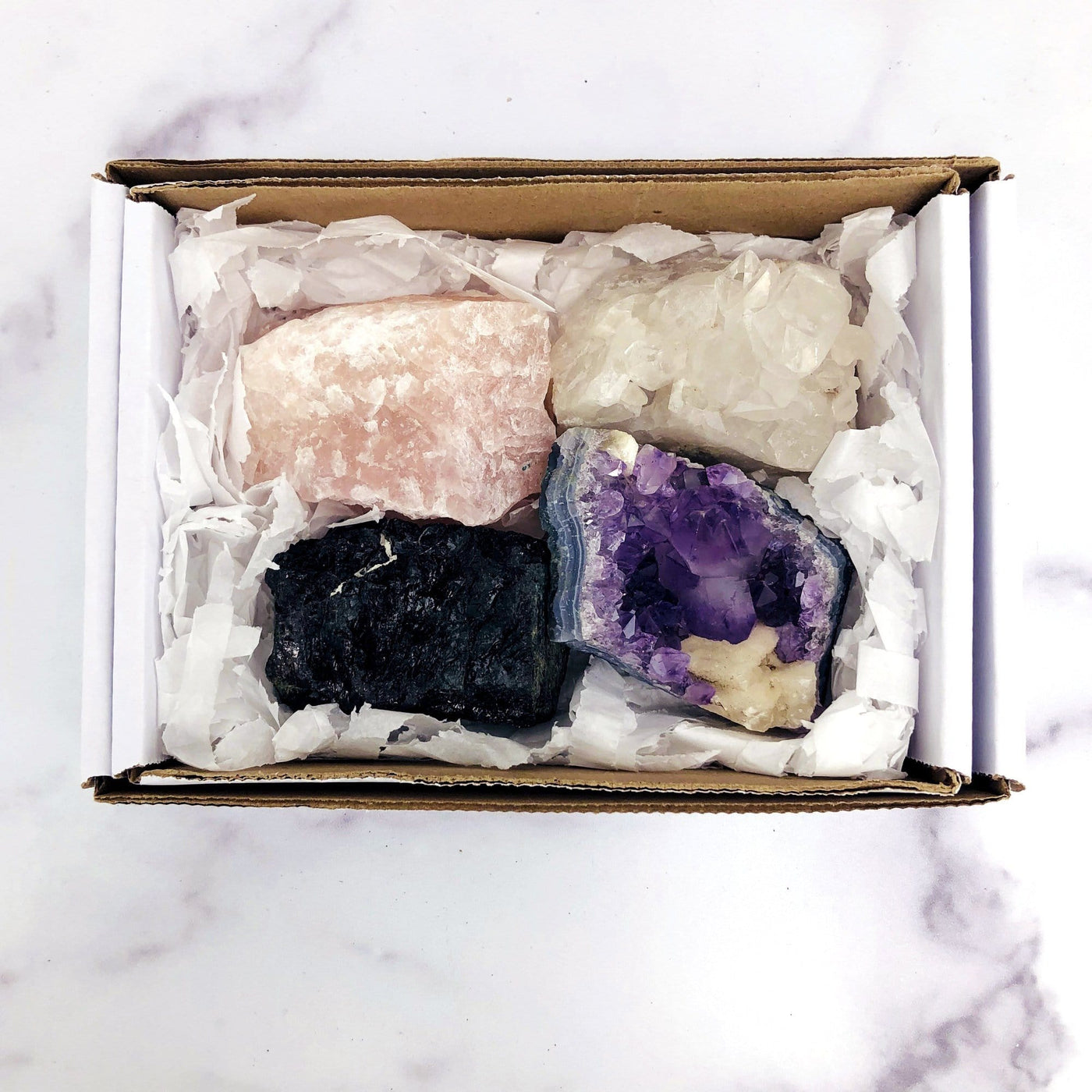 all four stones in a white box.  Box contains a rose quartz, crystal quartz cluster, black tourmaline, and amethyst cluster