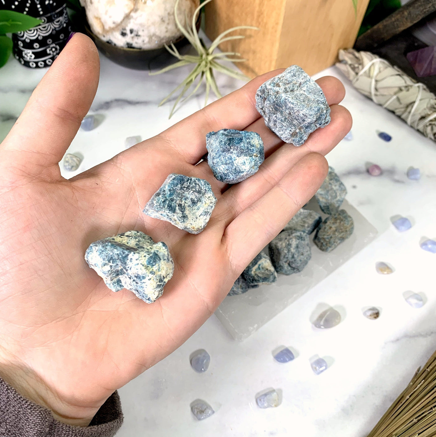 4 blue apatite stones in hand with white marble background
