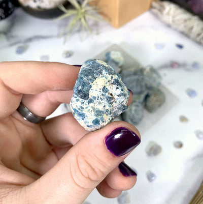 1 blue apatite stone in hand with marble background