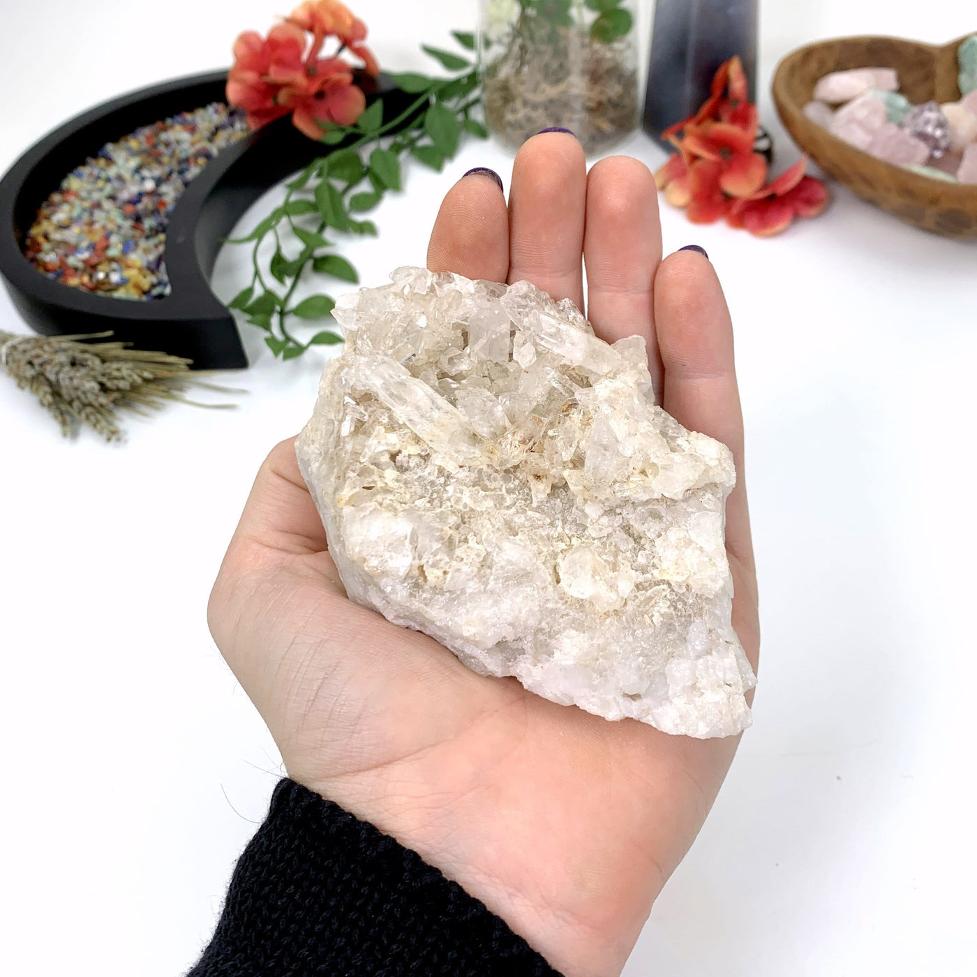 hand holding up Crystal Quartz Cluster with decorations in the background