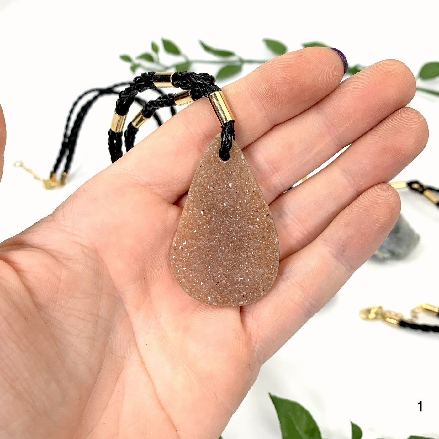 hand holding up Druzy Teardrop Shaped Necklace with decorations in the background