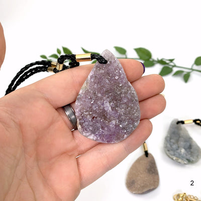 hand holding up Druzy Teardrop Shaped Necklace with decorations in the background