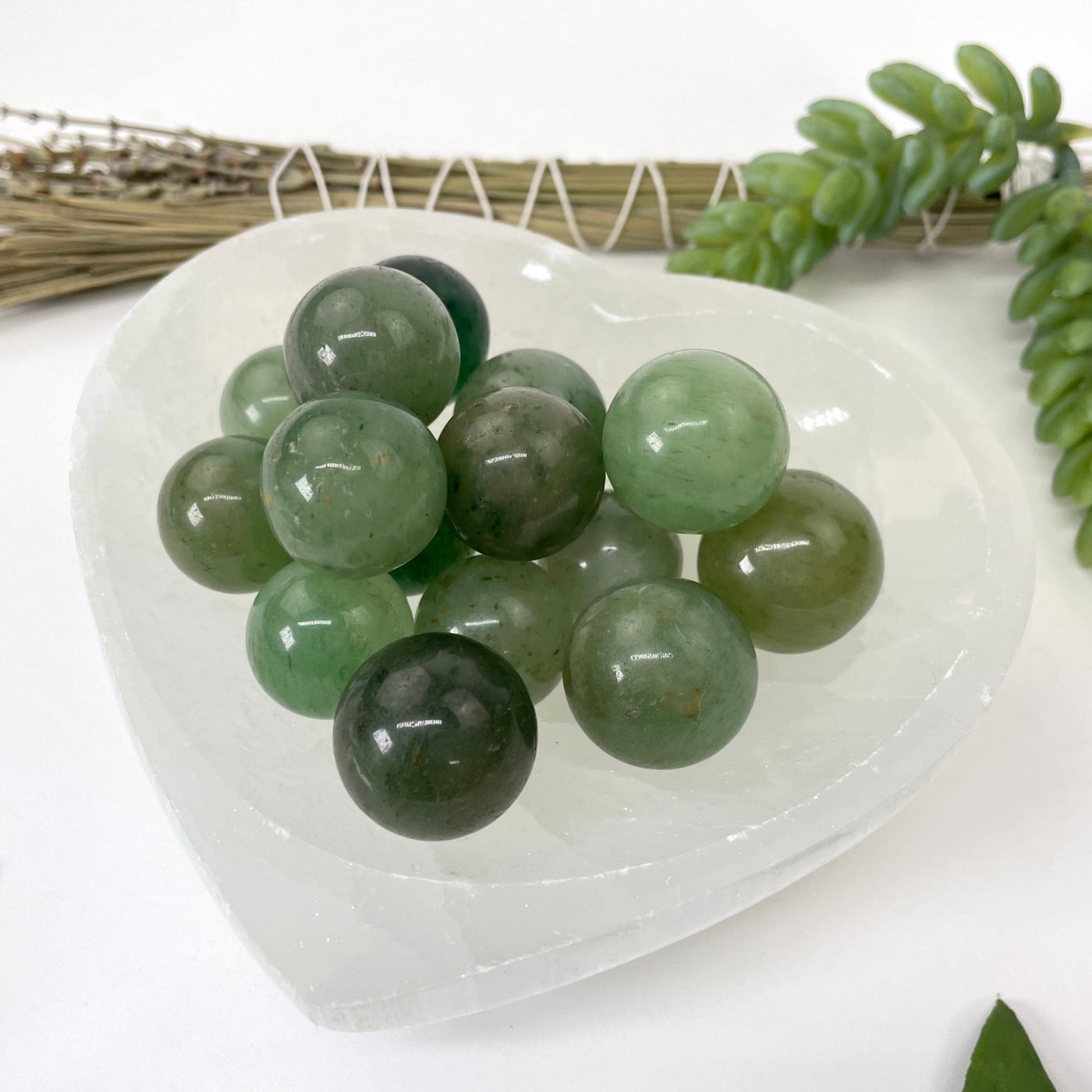 angled view of many green aventurine spheres in heart bowl for thickness