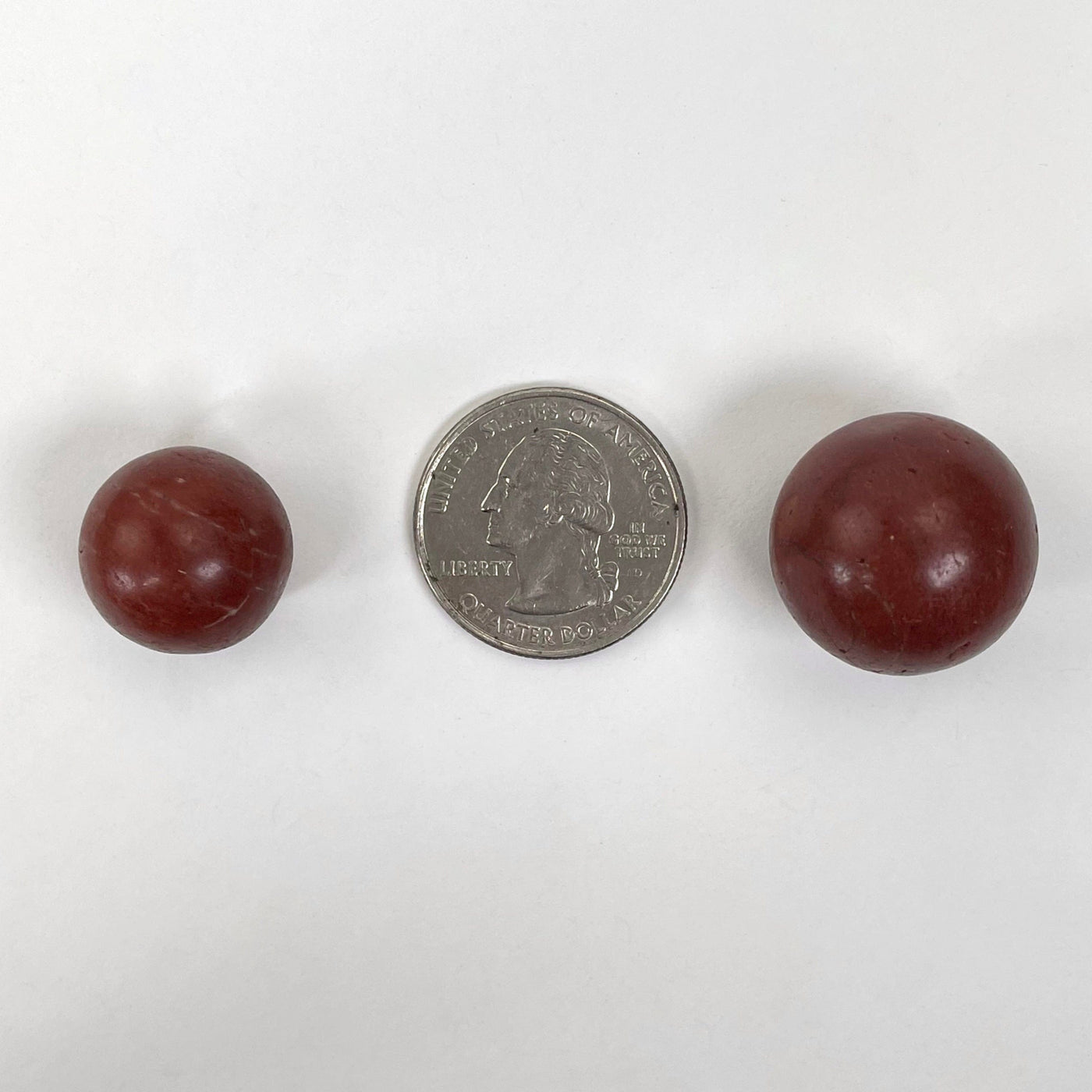 close up of two red jasper spheres on white background with quarter for size reference