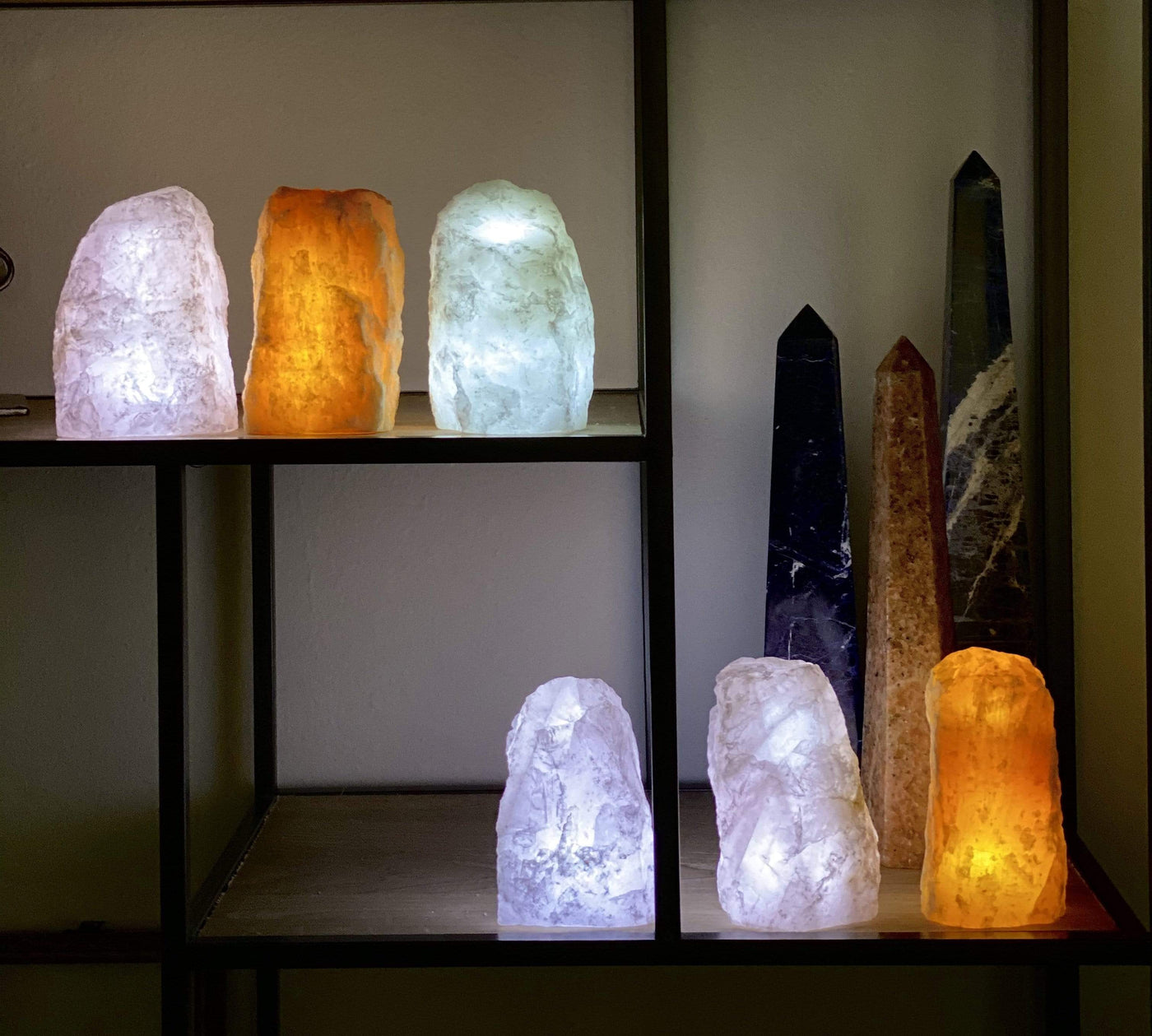 6 Rough Stone Lamps lit up in a dark room on a shelf with other crystals