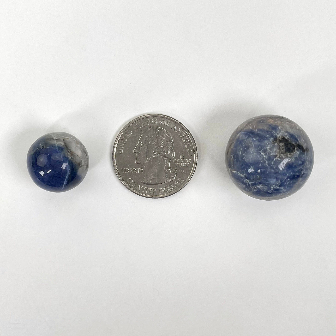 two sodalite sphere balls on white background with quarter for size reference