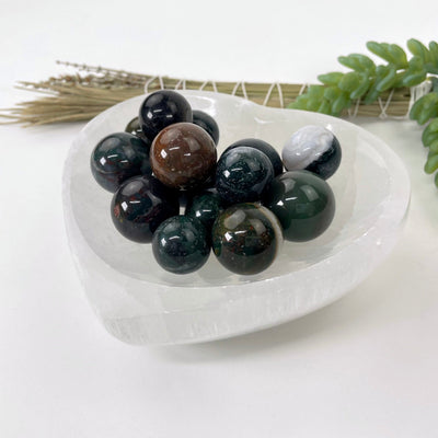 angled view of many bloodstone agate spheres in a heart bowl for thickness