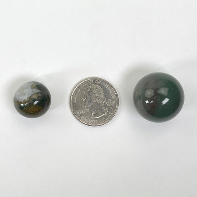 two bloodstone agate spheres on white background with quarter for size reference