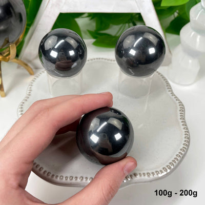 three 100g - 200g hematite polished spheres on display for possible variations with one in hand for size reference