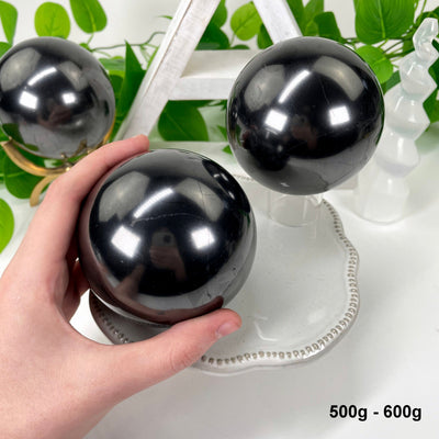 two 500g - 600g shungite polished spheres on display for possible variations with one in hand for size reference