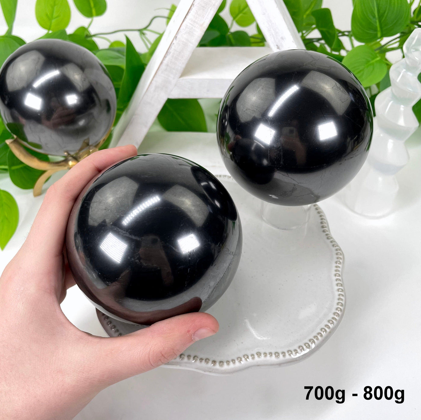 two 700g - 800g shungite polished spheres on display for possible variations with one in hand for size reference