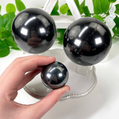 three different shungite polished sphere weights on display for size comparison with one in hand