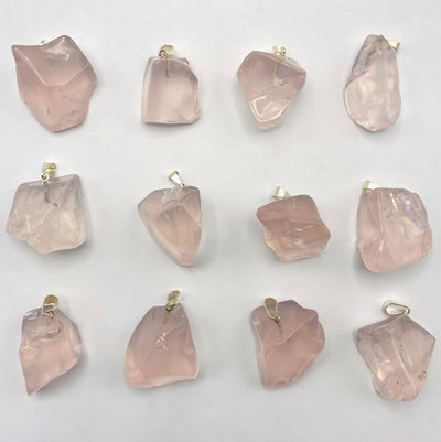 many tumbled rose quartz pendants in three rows on white background for possible variations