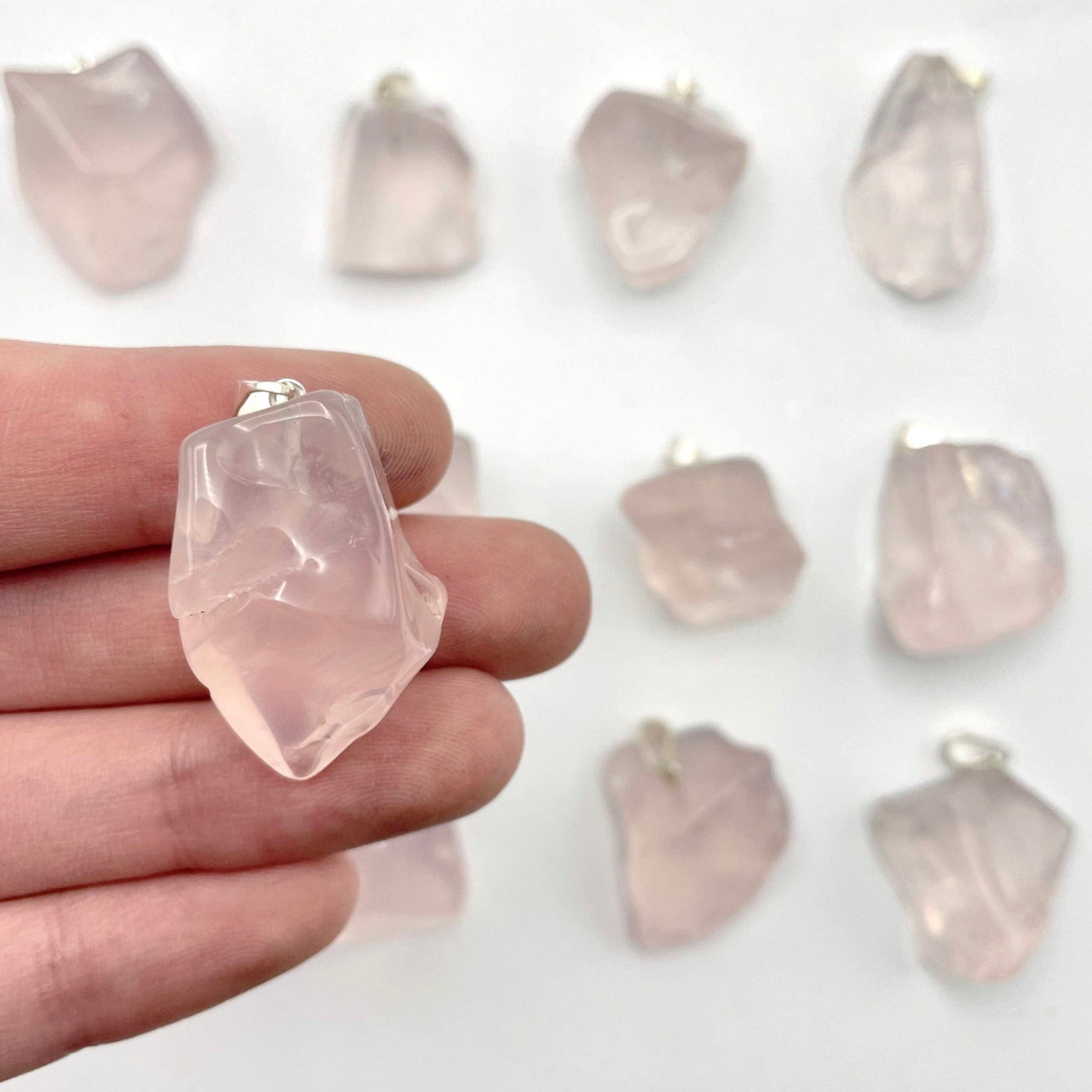 close up of one tumbled rose quartz pendant with silver bail in hand for size reference with many others in the background