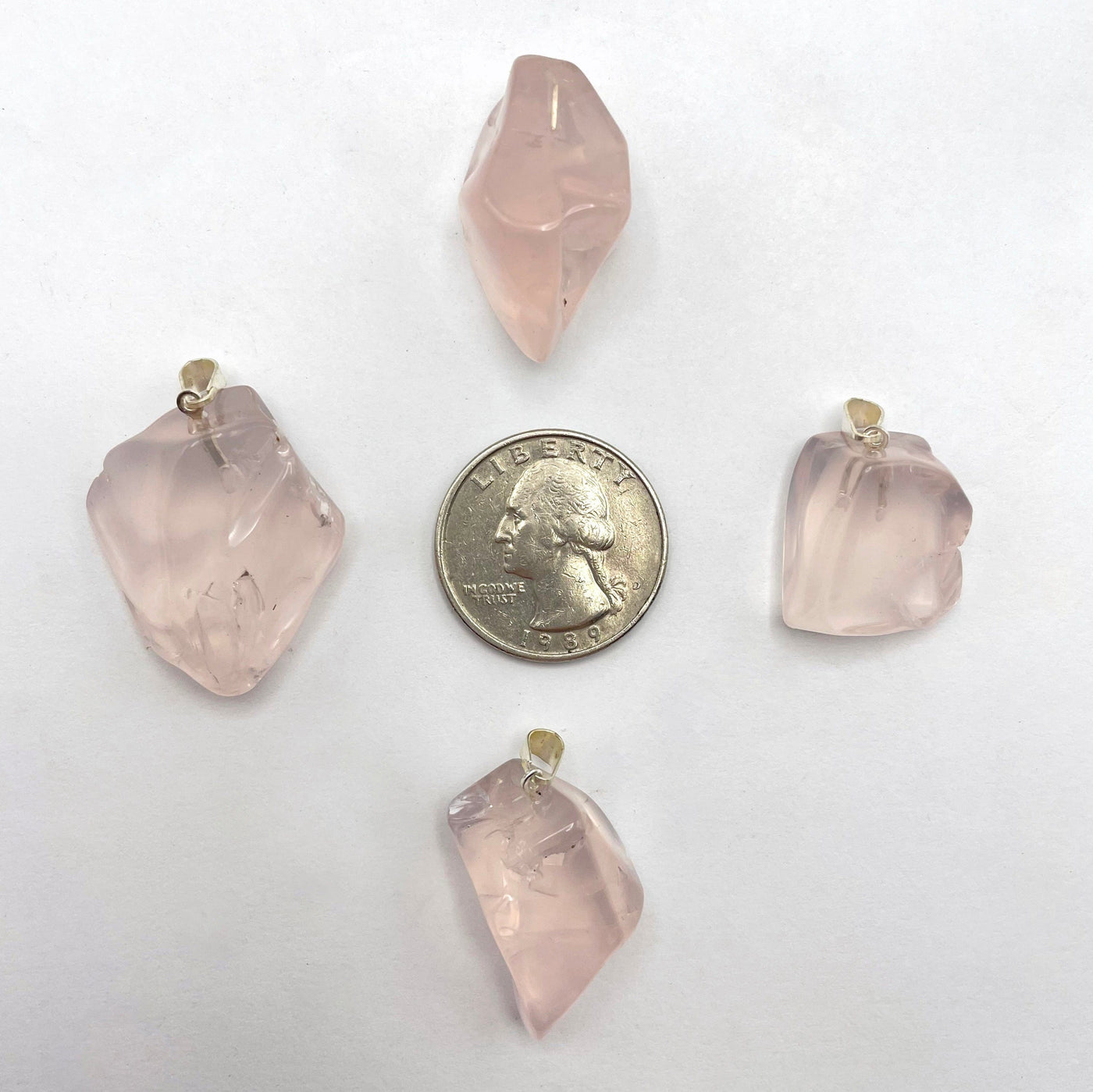 four tumbled rose quartz pendants on white background with quarter for size reference