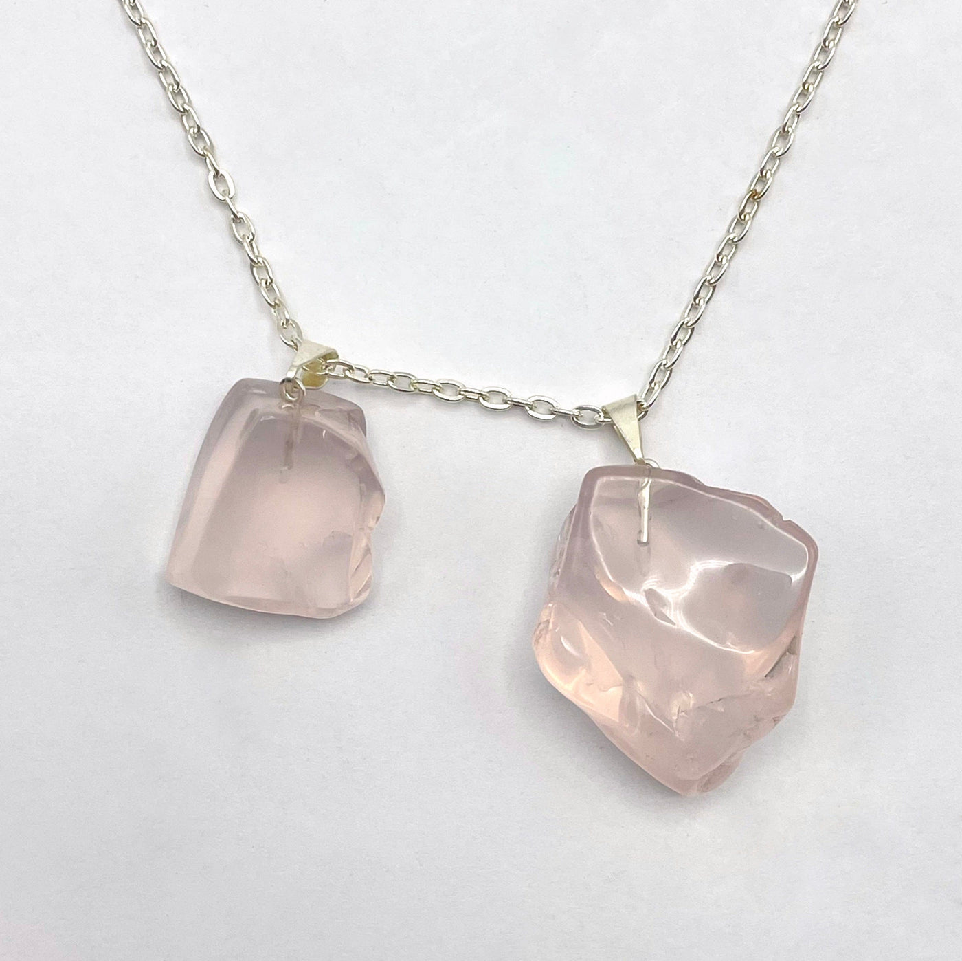 two tumbled rose quartz pendants on white background with silver chain strung through silver bail